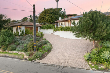 a paved driveway leads into a house with trees and bushes