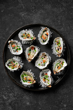 Freshly shucked oysters with buttermilk dressing, salmon roe, balsamic pearls and herb oil sitting on rock salt on a black plate