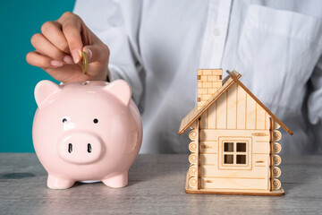 A woman puts a penny in a piggy bank, a wooden house on a table, savings to buy a house