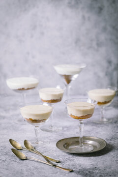 Arrangement of vanilla parfaits with cookie crumbles in vintage cocktail glasses on gray background and small silver plate