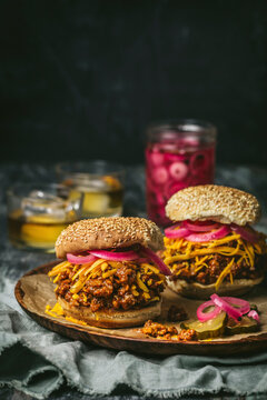 Front shot of Sloppy Joes (minced beef sandwiches) with cheddar cheese, pickled red onions on wood plate with pickle jar in background