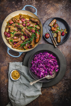 Dutch oven with sausages, potatoes, herbs, with bowl of bright red cabbage