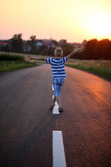 Cute baby boy running on the road at sunset. Happy childhood.