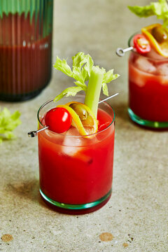 Bloody Mary Cocktail with Celery, Tomato & Olive Garnish on a Sage Green Surface