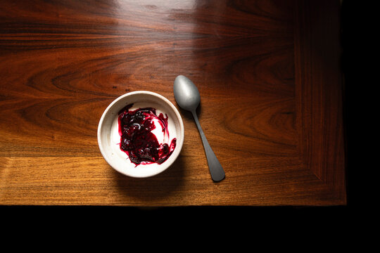 Bowl of yoghurt and blackberry compot on antinque wooden table with silver spoon.