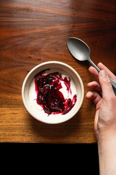 Bowl of yoghurt and blackberry compot on antinque wooden table with silver spoon.