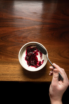 Bowl of yoghurt and blackberry compot on antinque wooden table with silver spoon.