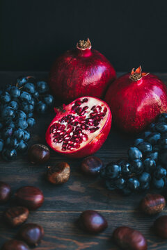 Autumn produce on a dark background, including grapes, chestnuts and pomegranate