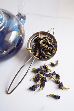 Blue butterfly pea flower tea on white marble background. Tea strainer with dried flowers closeup.