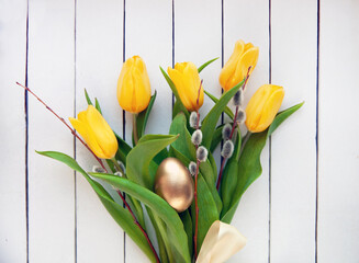 Easter concept. Bouquet of yellow tulips, willow branches with a golden egg.