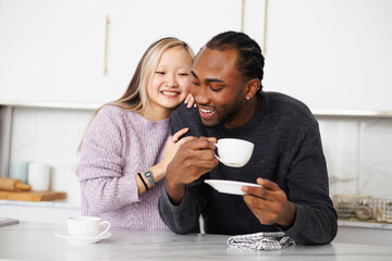Smiling young african american man holding cup near asian girlfriend in sweater at home