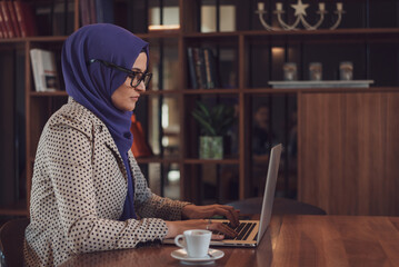 A happy young Muslim business woman in hijab working on a laptop at office