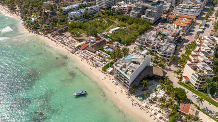 Aerial drone view of white sand beach with blue Caribbean Sea and hotel with rooftop pool surrounded by green vegetation on the coast of Playa del Carmen on a sunny afternoon