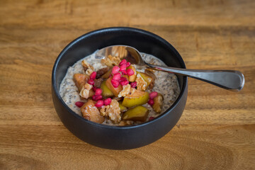 Healthy acai smoothie bowl with apple, sultanas, pomegranate seeds and walnuts in a black bowl with spoon on a wooden table