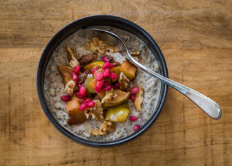 Top view of healthy acai smoothie bowl with apple, sultanas, pomegranate seeds and walnuts in a black bowl with spoon on a wooden table