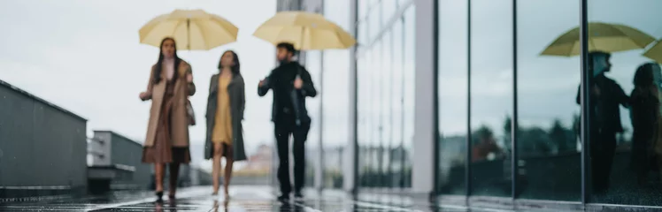 Fotobehang Three business individuals with umbrellas tread along a rain-drenched city sidewalk, reflection and urban life merging on a wet day. © qunica.com