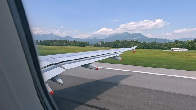 TIME LAPSE: The view from window as airplane reaches the runway and takes off. High alpine mountains and beautiful countryside dotted with villages and patterned with fields begin to appear below.