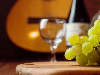 Green grapes in focus, glass and bottle of red wine and classic wooden guitar out of focus in the background.