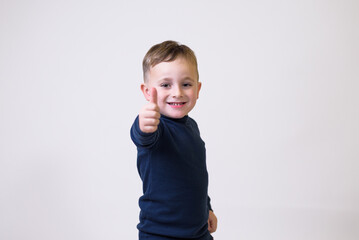 Portrait of cute boy in casual clothes showing thumbs up sign on white background