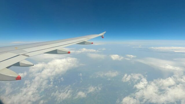 POV: A view of the wing from a passenger plane flying high above fluffy clouds. Traveling with modern and comfortable means of transport over heavenly cloudscape. Dreamy scenery during airplane flight