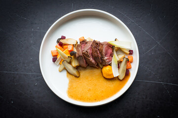 Slices of steak with mixed seasonal vegetables, mushrooms and gravy on a white plate on a dark background
