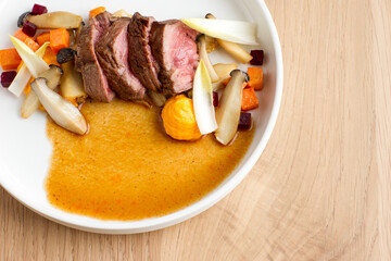 Slices of steak with mixed seasonal vegetables, mushrooms and gravy on a white plate on a wooden background
