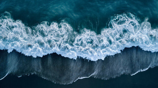 Aerial drone view or top view perspective photography of a beautiful transparent clear sea or ocean waves and foam splashing on the dark navvy blue or gray sand beach 