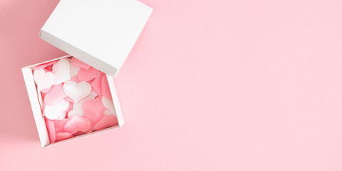 Pink background with pink and white hearts in an open gift box with a lid. Valentine's Day concept.