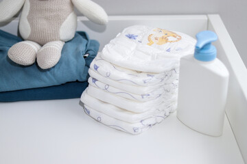Fototapeta na wymiar A stack of diapers, blue onesies and baby supplies on changing table