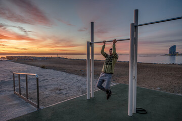 Man exercising in an outdoor gymnasium on the beach in Barcelona at first light of day.