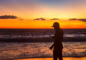 Fototapeta premium Man checking phone while enjoying beautiful sunset walking on the beach