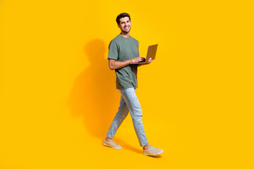 Full length photo of good mood funky guy wear khaki t-shirt walking communicating modern device isolated yellow color background