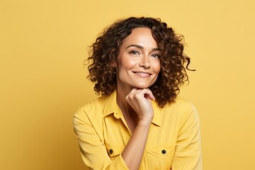 Portrait of beautiful young woman with curly hair looking at camera over yellow background