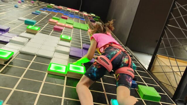 Motivated child navigates holds on climbing wall in fall arrest system. Small girl exhibits remarkable agility during climbing lesson