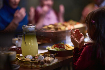 A young girl raises her hands in prayer as she prepares for her iftar meal during the holy month of...