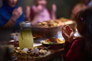A young girl raises her hands in prayer as she prepares for her iftar meal during the holy month of Ramadan, embodying spiritual devotion and innocence.