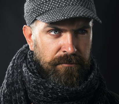 Closeup portrait serious bearded man in gray cap and scarf. Men fashion. Fashionable handsome man with beard and mustache in demi-season clothes. Winter knitwear. Fashion male model in winter outfit.