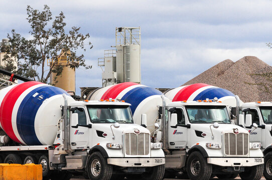 At a Cemex Concrete Plant in Pinal County, Arizona, ready-mix cement trucks, a large pile of sand, and processing silos are showcased at the facility