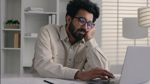 Arabian Indian ethnic male tired businessman office employee boring work with laptop dreary exhausted lazy bored business man low energy overworked fatigue depression apathy burnout typing on computer