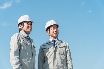 青空の中に立つ作業服を着た作業員（建設・建築・設計・不動産・土木・工事・現場監督・運送）
