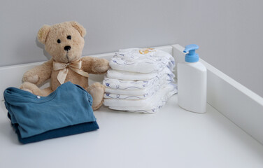 A stack of diapers, onesies, teddy bear and baby supplies on changing table