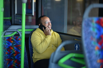 a lustful dark-skinned young man is sitting in the bus and talking on the phone - obrazy, fototapety, plakaty