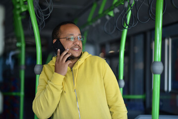 a lustful dark-skinned young man is sitting in the bus and talking on the phone - obrazy, fototapety, plakaty