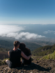 Naklejka na ściany i meble romantic lovely couple sitting on mountain top above clouds and looking on view