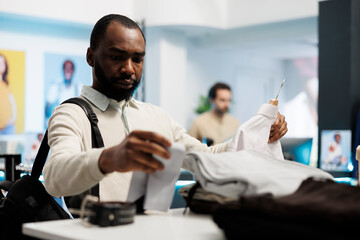 African american man holding shirt, examining style and fabric quality in clothing store. Customer looking at formal apparel on hanger while shopping in mall menswear department
