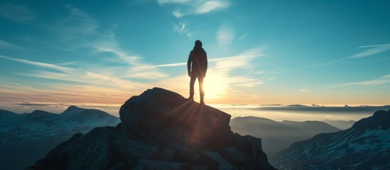 A person stands on a mountain at sunset, admiring the breathtaking natural landscape, as clouds float across the colorful sky.
