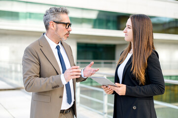 Senior businessman and his junior associate stand side by side, engaged in a serious business...