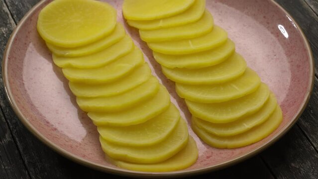 Turmeric pickled daikon (takuan) on pink plate rotating in a circle. Wooden rustic table. 