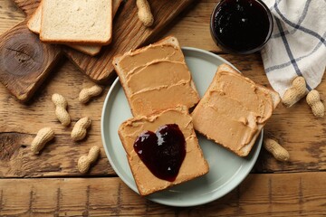 Tasty peanut butter sandwiches with jam and peanuts on wooden table, flat lay