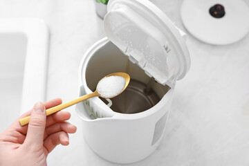 Cleaning electric kettle. Woman adding baking soda to appliance at table, above view